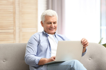 Portrait of mature man with laptop on sofa indoors