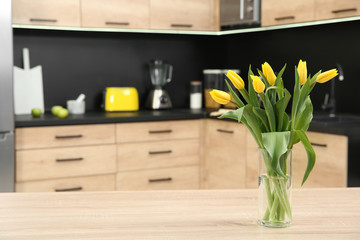 Glass vase with tulips on table in kitchen