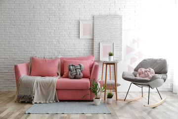 Stylish living room interior with sofa and rocking armchair near brick wall. Space for text