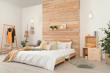 Stylish room interior with comfortable bed near wooden wall