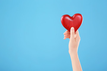 Woman holding decorative heart in hand on color background, space for text