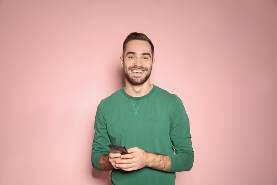 Handsome young man with mobile phone on color background