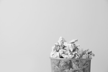 Metal bin with crumpled paper against light background, space for text