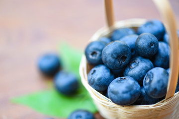 Fresh blueberries fruit in basket and green leaves on wooden background