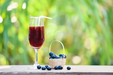 Blueberry smoothie juice glass and fresh blueberries fruit in basket with nature green summer background