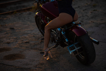 Red-haired woman in sexy lingerie in high heels sits on a motorcycle. Attractive red-haired girl sits on a motorcycle at sunset on the background of the industrial landscape