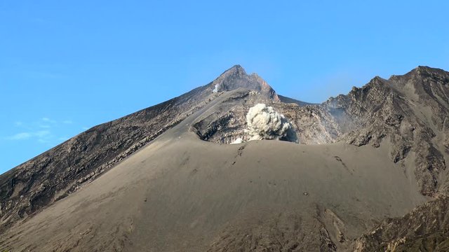 View of Sakurajima volcanic mountain peaks against blue sky erupting with volcanic ash clouds slow motion, Kagoshima, Japan