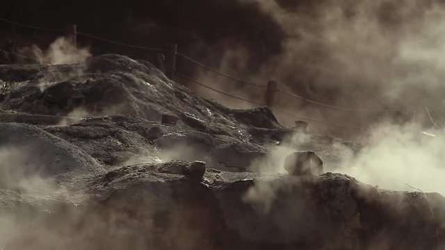 Steaming volcanic gas clouds blowing over Owakudani Hell Valley black rocky grounds with rope walk trail in background.