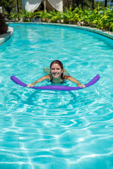 A young woman learns to swim in an outdoor pool using a swimming noodle.