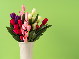 Colorful tulips in vase on white table wall green background