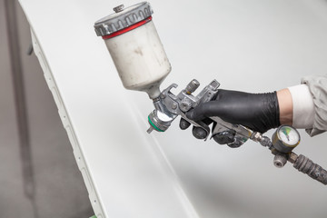 A male worker paints with a spray gun a part of the car body in silver after being damaged at an...