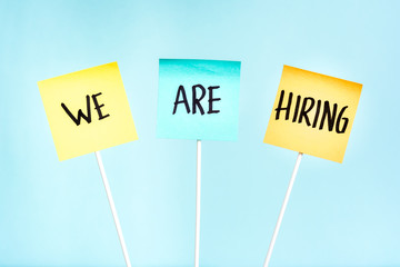 Three notes with the text "we are hiring" on plank holder. Concept of employment, search job and recruitment process.