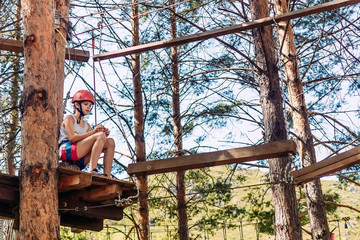 ten-year-old girl in a helmet on a rope town outdoors in the summer. Rest before the passage of obstacles. To overcome fear