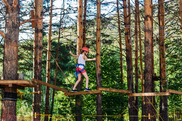 a ten-year-old girl in shorts, a t-shirt and a protective helmet is on a rope Park . Extreme sports on top.