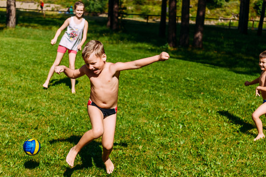 Children Playing Dodgeball With The Ball On The Green Lawn In The Summer