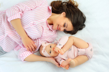Mom and 8-month-old baby hugging on the bed in pink clothes