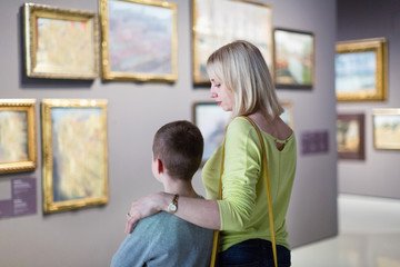 Mother and son regarding paintings in halls of museum
