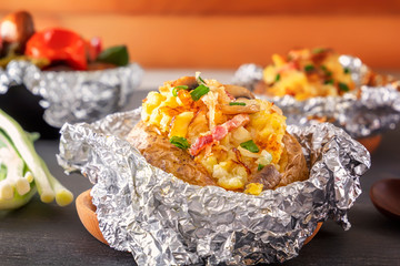 Baked potato in foil with bacon, onions and mushrooms on a gray wooden table.Copy space. Close-up