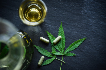 Marijuana leaf plant cannabis herbal tea and capsule on dark background / Hemp leaves for extract...