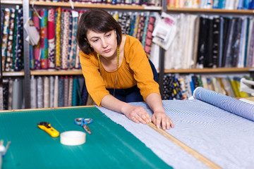 Saleswoman measuring and cutting off piece of cloth