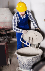 Young smiling male using concrete mixer at workshop
