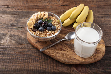 granola with banana, berries and glass of milk on wooden background