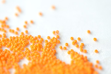 Opaque seed beads orange color scattered on a textile background close up
