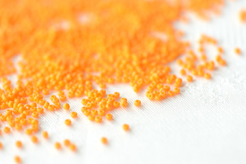 Opaque seed beads orange color scattered on a textile background close up