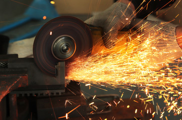a gloved worker with a grinder cuts a carbide plate and this causes a lot of sparks