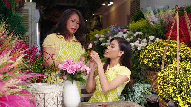 Medium shot of elderly Asian woman showing young Asian trainee how to make flowers bunch