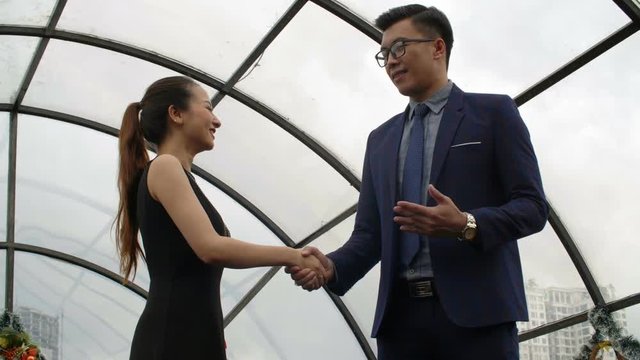 Medium shot of Asian businessman and businesswoman shaking hands and discussing terms of transaction