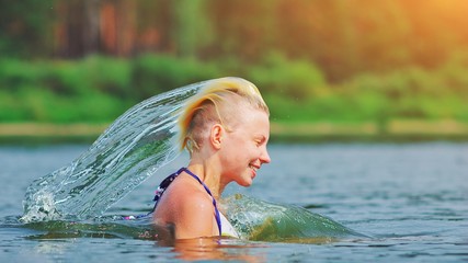 Active young blonde woman splashing water in river. Beautiful healthy lady in water waving hair, relax and laughing, raising head out of the water Vacation in paradise enjoying swimming Motion freeze