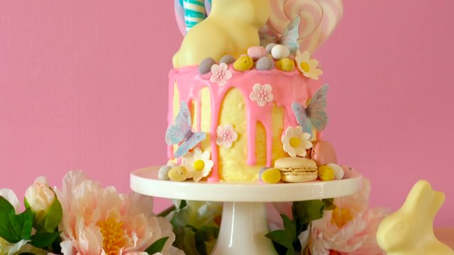 On trend Easter candy land drip cake decorated with lollipops, cand eggs and white chocolate bunny in pink party table setting.