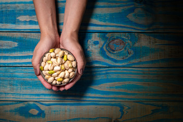 Brunette model holding ceramic pot with pistachios on blue wooden background.