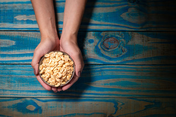 Brunette model holding ceramic pot with roasted peanuts on blue wooden background.