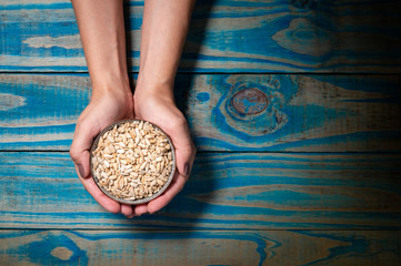 Brunette model holding pot of ceramic with roasted sunflower seed, blue wooden background.
