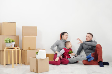 Young family, man woman and child son sits at floor in new apartments. Boxes with cargo on a white background.