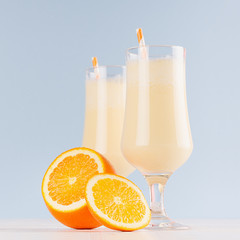 Sweety dairy yogurt of oranges with striped straw, cut orange on soft light blue background, square.