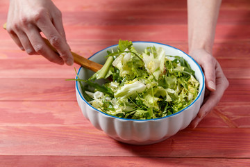 Fresh vegetarian salad from escariol, frieze, radicio, arugula in a white plate on a wooden background.