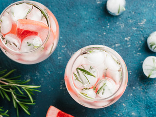 infused detox water or alcoholic or non-alcoholic cocktail with grapefruit and rosemary ice in glass on green cement background. healthy eating or holyday drink concept, copy space for text. Top view