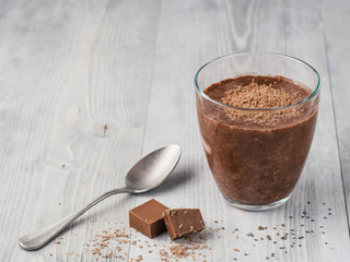 Chocolate chia pudding in glass and chocolate cubes slice on gray wooden table. Healthy vegan...