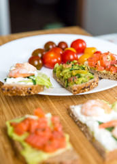 Open sandviches with guacamole, salmon and shrimp and tomato cherry on the plate, wooden background