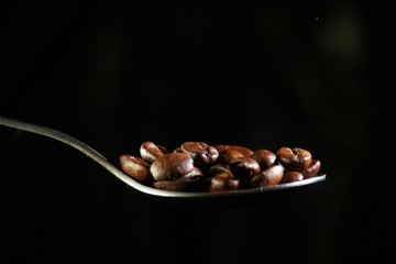 A spoon with coffee beans at dark background