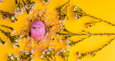 Top view Easter pink egg in the nest on yellow paper background with flowers