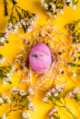 Top view Easter pink egg in the nest on yellow paper background with flowers