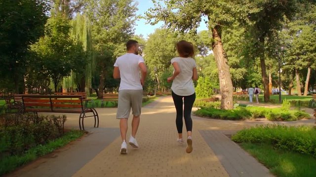unrecognizable couple woman with blond hair and man wearing white t-shirt running in city park. healthy lifestyle jog in summer season day time cardio workout outdoor