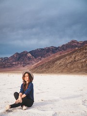 Fototapeta na wymiar Brunette girl in a plaid shirt with long hair and a gray hat on saline soil Badwater in Death Valley