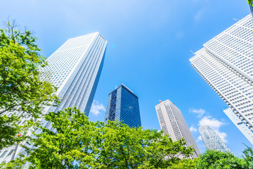 Asia Business concept for real estate, corporate construction and ecology - looking up view of panoramic modern city skyline with blue sky and green tree in shinjuku, tokyo, japan