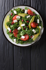 Fresh salad of kale, avocado, grapefruit, cheese and dried cranberries close-up on a plate. Vertical top view
