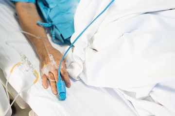 Close up old woman patient hand and iv set for fluid intravenous drop saline drip on white hospital bed background in the hospital room.Medical treatment emergency patient.Seriously patient admitted